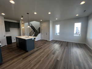 Kitchen with dishwasher, sink, hanging light fixtures, dark wood-type flooring, and a center island with sink