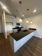 Kitchen with gas stove, sink, dark stone countertops, white cabinets, and hanging light fixtures