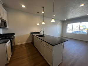 Kitchen with hanging light fixtures, sink, appliances with stainless steel finishes, dark hardwood / wood-style flooring, and white cabinetry