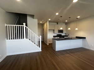 Kitchen featuring stainless steel appliances, dark wood-type flooring, sink, pendant lighting, and white cabinetry