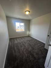 Empty room featuring a textured ceiling and dark colored carpet