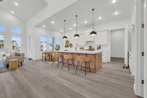 Kitchen featuring a breakfast bar, decorative light fixtures, white cabinetry, a kitchen island with sink.