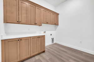 Clothes washing area with cabinets, washer hookup, hookup for an electric dryer, and light hardwood / wood-style flooring