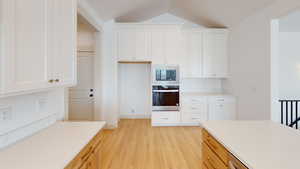 Kitchen with white cabinetry, built in microwave, lofted ceiling, and stainless steel oven