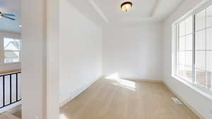 Empty room featuring a tray ceiling, ceiling fan, and light colored carpet