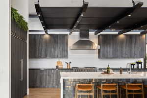 Kitchen featuring sink, light hardwood / wood-style flooring, wall chimney exhaust hood, a kitchen bar, and stainless steel gas cooktop