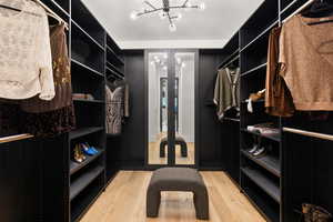 Walk in closet with an inviting chandelier and light hardwood / wood-style flooring