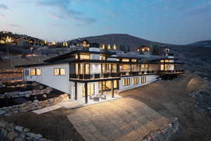 Back house at dusk with a mountain view, a balcony, and a patio area