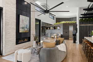 Living room with a stone fireplace, ceiling fan, light hardwood / wood-style floors, and a high ceiling