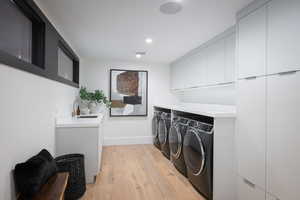 Clothes washing area with cabinets, washing machine and dryer, light hardwood / wood-style floors, and sink