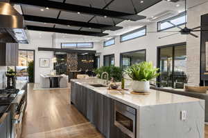 Kitchen with light stone countertops, a large island with sink, appliances with stainless steel finishes, and a high ceiling