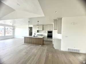 Kitchen with vaulted ceiling, sink, pendant lighting, a center island with sink, and hardwood / wood-style floors