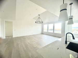 Unfurnished living room featuring sink, light hardwood / wood-style flooring, a notable chandelier, a textured ceiling, and vaulted ceiling