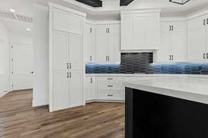 Kitchen featuring backsplash, hardwood / wood-style flooring, white cabinetry, and light stone counters