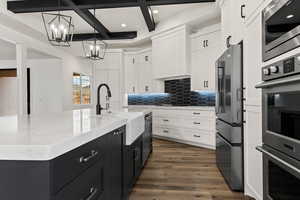 Kitchen featuring pendant lighting, a kitchen island with sink, coffered ceiling, beam ceiling, and stainless steel appliances