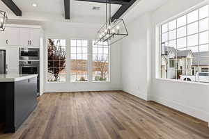 Unfurnished dining area featuring a chandelier, beam ceiling, and light hardwood / wood-style flooring