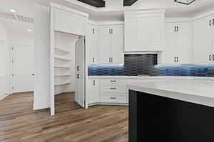 Kitchen with decorative backsplash, wood-type flooring, white cabinetry, and light stone counters