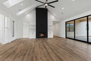 Unfurnished living room featuring a large fireplace, wood-type flooring, high vaulted ceiling, and a skylight