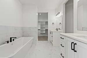 Bathroom featuring a tub to relax in, vanity, and tile walls