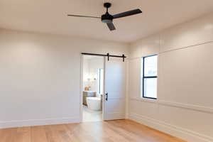 Empty room with a barn door, ceiling fan, and light hardwood / wood-style floors