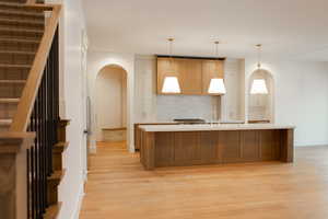 Kitchen with sink, hanging light fixtures, tasteful backsplash, light hardwood / wood-style floors, and a kitchen island with sink