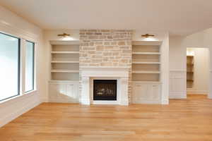 Unfurnished living room featuring built in shelves, light hardwood / wood-style floors, and a healthy amount of sunlight