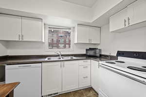 Kitchen with dark tile patterned flooring, white appliances, white cabinetry, and sink