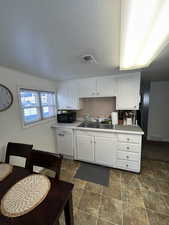 Kitchen with white dishwasher, white cabinets, and sink