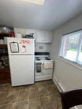 Kitchen featuring white cabinets, white appliances, and baseboard heating