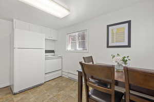 Kitchen featuring white cabinets, stove, white fridge, and a baseboard radiator