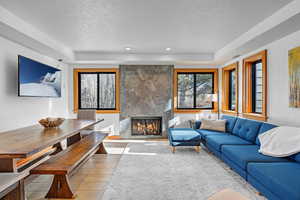 Living room with a raised ceiling, a fireplace, a textured ceiling, and light wood-type flooring