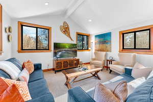 Carpeted living room featuring vaulted ceiling with beams and plenty of natural light