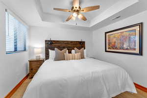 Bedroom with a tray ceiling, ceiling fan, and light hardwood / wood-style flooring