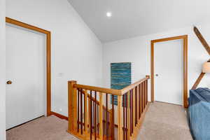 Hallway featuring light carpet and vaulted ceiling