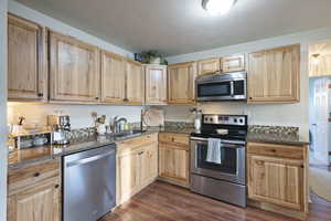 Kitchen featuring dark hardwood / wood-style flooring, appliances with stainless steel finishes, and dark stone counters