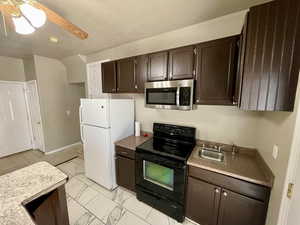 Kitchen with dark brown cabinetry, ceiling fan, sink, white refrigerator, and black / electric stove