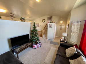 Carpeted living room with a textured ceiling, vaulted ceiling, and ceiling fan