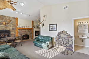 Carpeted living room with a stone fireplace, sink, track lighting, and lofted ceiling