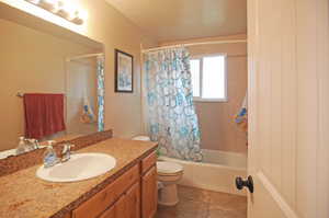 Full bathroom with vanity, tile patterned flooring, toilet, shower / bath combo with shower curtain, and a textured ceiling