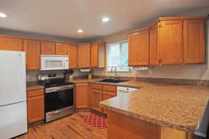 Kitchen featuring kitchen peninsula, light wood-type flooring, white appliances, and sink