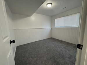 Empty room with dark colored carpet, a textured ceiling, and wood walls