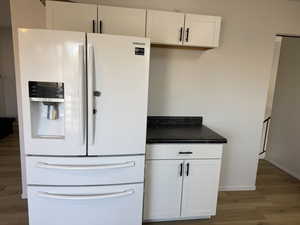 Kitchen with white cabinets, white refrigerator with ice dispenser, and hardwood / wood-style flooring