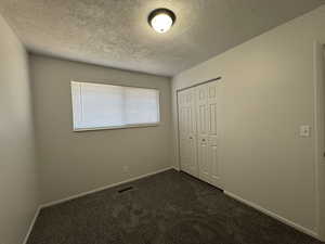 Unfurnished bedroom featuring a closet, dark carpet, and a textured ceiling