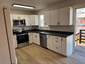 Kitchen with a wealth of natural light, white cabinetry, sink, and appliances with stainless steel finishes