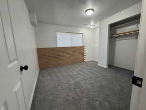 Unfurnished bedroom featuring a textured ceiling, dark carpet, and a closet