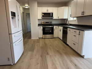 Kitchen featuring white cabinets, light wood-type flooring, stainless steel appliances, and sink