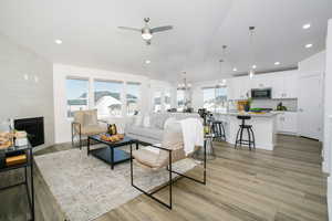 Living room with a tile fireplace, plenty of natural light, ceiling fan with notable chandelier, and light hardwood / wood-style flooring