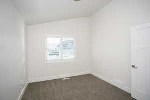 Spare room with dark carpet and lofted ceiling