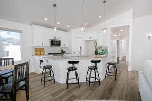 Kitchen with white cabinetry, dark hardwood / wood-style floors, pendant lighting, lofted ceiling, and a kitchen island with sink