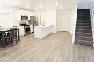 Kitchen featuring light wood-type flooring, stainless steel appliances, sink, white cabinets, and hanging light fixtures